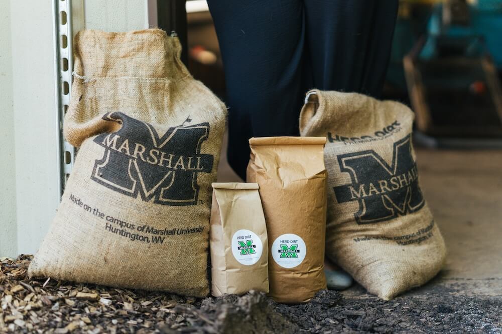 Bags of Marshall University's Herd Dirt Premium Compost are displayed outside the university's composting facility.