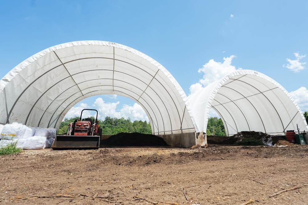 The covered composting area at Marshall University's commercial composting facility, with equipment and compost storage beneath large fabric structures.